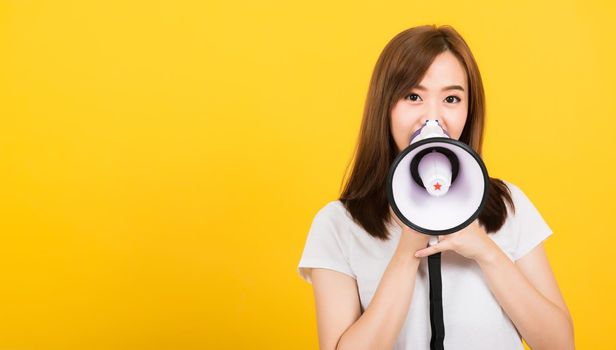 Asian happy portrait beautiful cute young woman teen standing making announcement message shouting screaming in megaphone looking to camera isolated, studio shot on yellow background with copy space