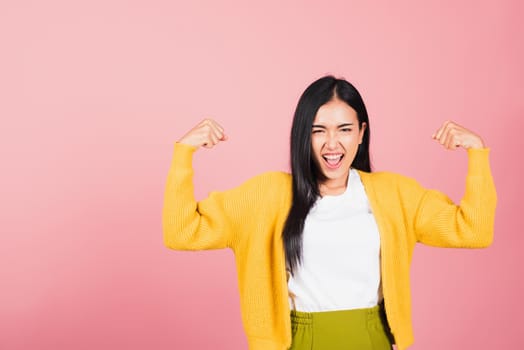 Portrait Asian of happy beautiful strong muscles young woman raises arms biceps confident showing power and strength have feeling independent victory successful, studio shot isolated pink background