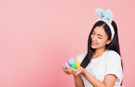 Happy Easter concept. Beautiful young woman smiling wearing rabbit ears holding colorful Easter eggs gift on hands, Portrait female looking at eggs, studio shot isolated on pink background