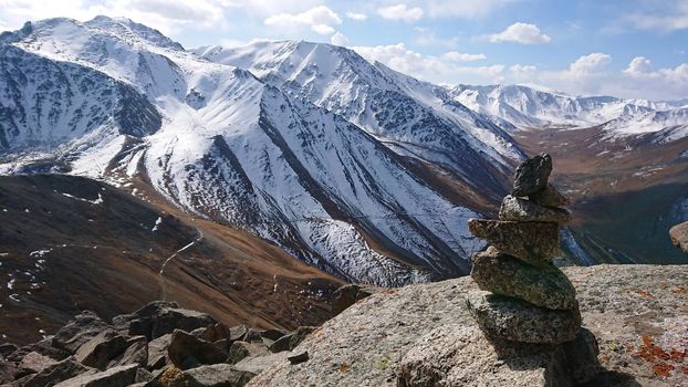 A pile of stones points the way. The stones of the pyramid indicate the direction of tourists. View of snowy mountains, gorges and sky with clouds. Panorama for the desktop.