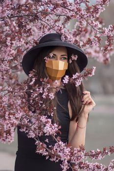 Portrait of a young woman in the spring flowers of a tree. A girl in a medical mask. Polygonal medical mask.