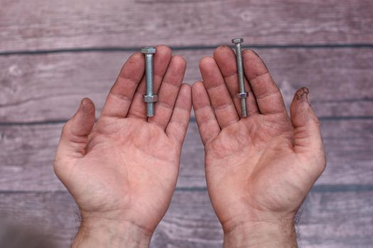 two bolts and nuts in working men's hands. On a wooden background.