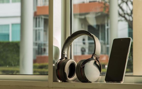 Smartphone and Headphones for listening to music Placed on glass wall In the time of rest. Personal device with Space for text. Selective focus.