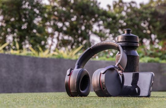 Composition of Smartphone and Headphones for listening to music and water bottle Placed on green grass In the time of rest, Summer lawn with personal device with Space for text.