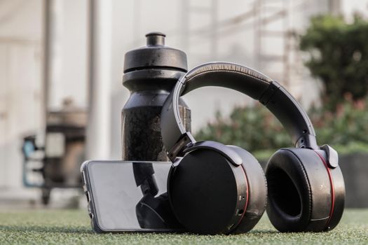 Composition of Smartphone and Headphones for listening to music and water bottle Placed on green grass In the time of rest, Summer lawn with personal device with Space for text.
