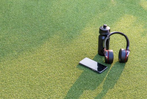 Composition of Smartphone and Headphones for listening to music and water bottle Placed on green grass In the time of rest, Summer lawn with personal device with Space for text.
