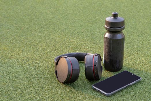 Composition of Smartphone and Headphones for listening to music and water bottle Placed on green grass In the time of rest, Summer lawn with personal device with Space for text.