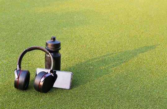 Composition of Smartphone and Headphones for listening to music and water bottle Placed on green grass In the time of rest, Summer lawn with personal device with Space for text.