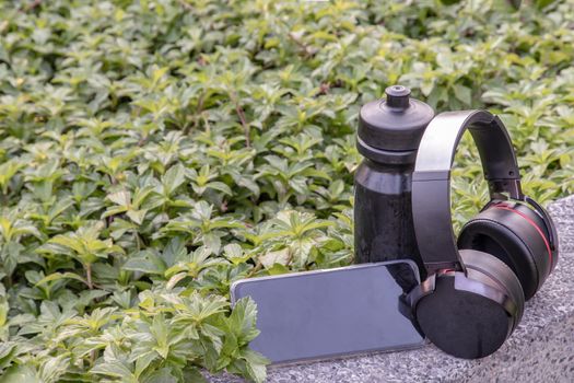 Composition of Smartphone and Headphones for listening to music and water bottle Placed on natural green background In the time of rest. Personal device with Space for text, Selective focus.