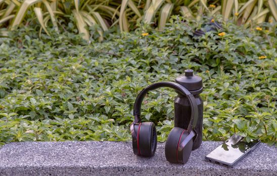 Composition of Smartphone and Headphones for listening to music and water bottle Placed on natural green background In the time of rest. Personal device with Space for text, Selective focus.