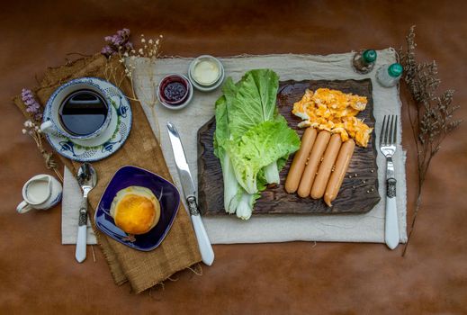 Continental breakfast with scrambled eggs, fried sausages, vegetable and scones served with coffee with milk. Wood background, Selective focuse.