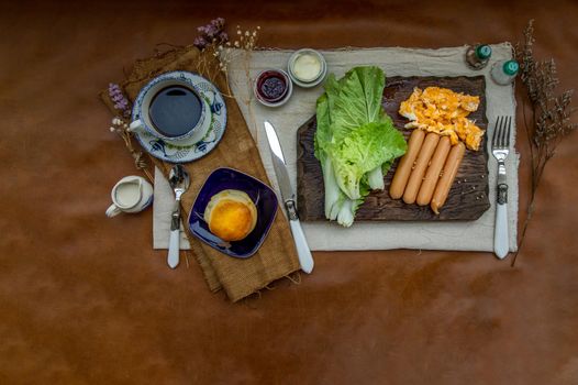 Continental breakfast with scrambled eggs, fried sausages, vegetable and scones served with coffee with milk. Wood background, Selective focuse.