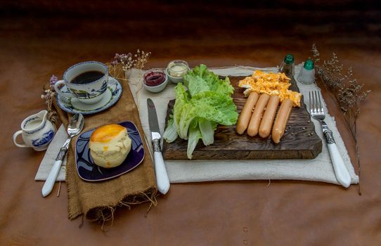 Continental breakfast with scrambled eggs, fried sausages, vegetable and scones served with coffee with milk. Wood background, Selective focuse.