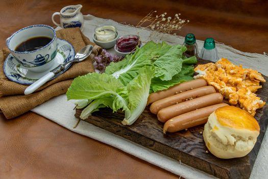 Continental breakfast with scrambled eggs, fried sausages, vegetable and scones served with coffee with milk. Wood background, Selective focuse.