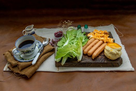 Continental breakfast with scrambled eggs, fried sausages, vegetable and scones served with coffee with milk. Wood background, Selective focuse.