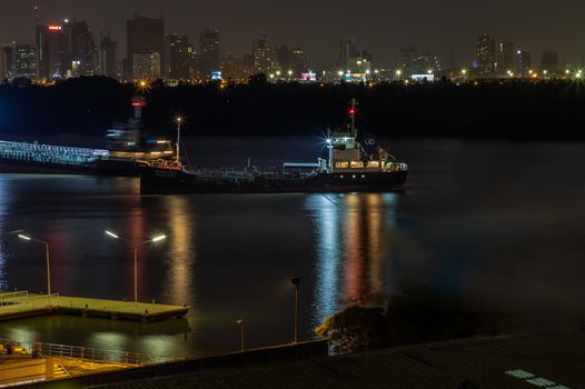 Bangkok, Thailand - 09 Apr 2020 : Cargo ship parked in the middle of the Chao praya river and Beautiful view of Bangkok city in the night.