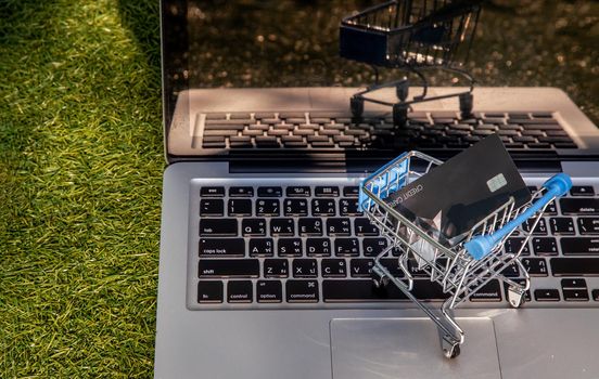 A credit card in a Mini supermarket trolley on a laptop keyboard. E-commerce and online shopping concept. Ideas about home shopping or buying things in virtual malls / stores from home or office by using modern technology called internet and web browser.