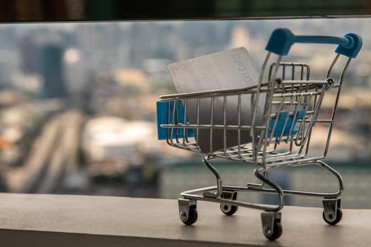 A credit card in a Mini supermarket trolley on Cityscape background. Ideas about home online shopping.
