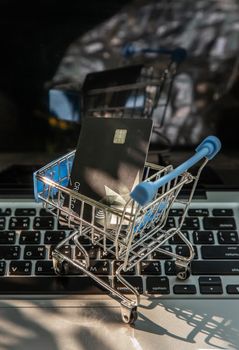 A credit card in a Mini supermarket trolley on a laptop keyboard. E-commerce and online shopping concept. Ideas about home shopping or buying things in virtual malls / stores from home or office by using modern technology called internet and web browser.