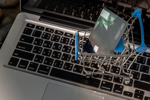 A credit card in a Mini supermarket trolley on a laptop keyboard. E-commerce and online shopping concept. Ideas about home shopping or buying things in virtual malls / stores from home or office by using modern technology called internet and web browser.