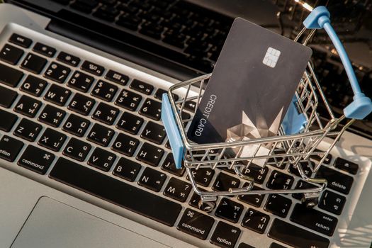 A credit card in a Mini supermarket trolley on a laptop keyboard. E-commerce and online shopping concept. Ideas about home shopping or buying things in virtual malls / stores from home or office by using modern technology called internet and web browser.