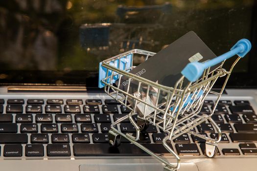 A credit card in a Mini supermarket trolley on a laptop keyboard. E-commerce and online shopping concept. Ideas about home shopping or buying things in virtual malls / stores from home or office by using modern technology called internet and web browser.