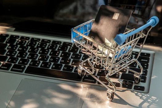 A credit card in a Mini supermarket trolley on a laptop keyboard. E-commerce and online shopping concept. Ideas about home shopping or buying things in virtual malls / stores from home or office by using modern technology called internet and web browser.