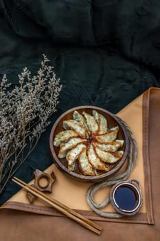 Fried japanese gyoza dumplings on wooden bowl served with soy sauce and chopsticks. Asian dinner, Top view, Selective focus.
