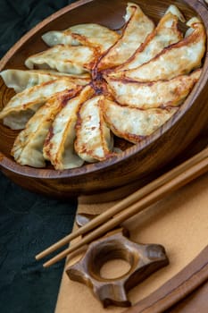 Fried japanese gyoza dumplings on wooden bowl served with soy sauce and chopsticks. Asian dinner, Selective focus.