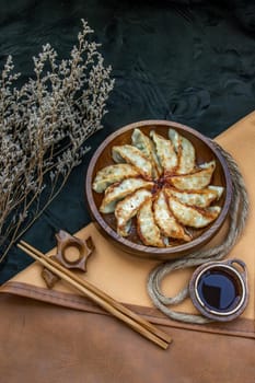 Fried japanese gyoza dumplings on wooden bowl served with soy sauce and chopsticks. Asian dinner, Top view, Selective focus.