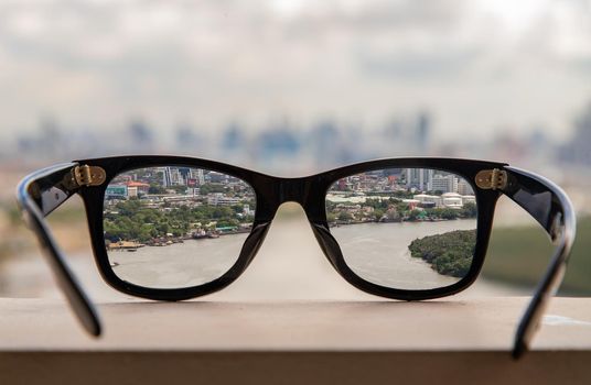 Bangkok, Thailand - Jun 09 2020 :  Black eyeglass on a reflective surface. View through the lens of glasses that look at the Chao Phraya River.