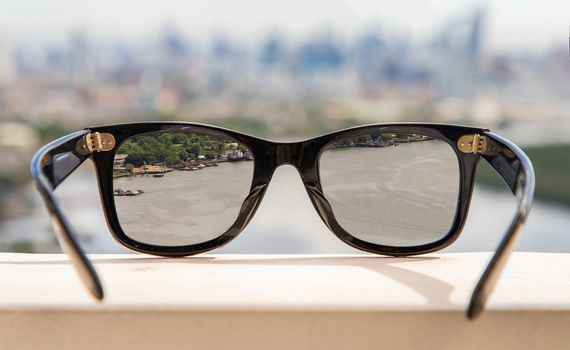 Bangkok, Thailand - Jun 09 2020 :  Black eyeglass on a reflective surface. View through the lens of glasses that look at the Chao Phraya River.