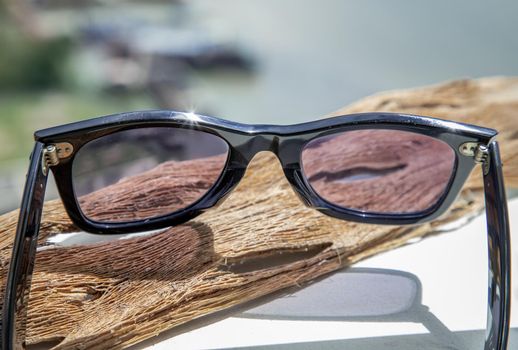 Black eyeglass on a reflective surface on wooden background in the afternoon.