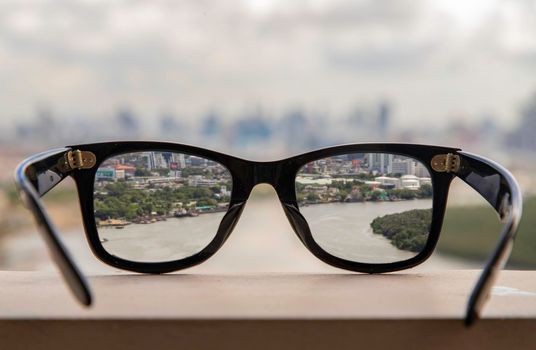 Bangkok, Thailand - Jun 09 2020 :  Black eyeglass on a reflective surface. View through the lens of glasses that look at the Chao Phraya River.