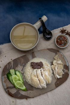 Hainanese chicken rice (Steam chicken with rice) with cucumber closeup on a plate and broth. Horizontal top view.