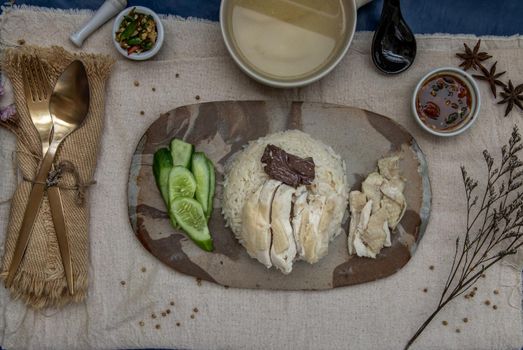Hainanese chicken rice (Steam chicken with rice) with cucumber closeup on a plate and broth. Horizontal top view.