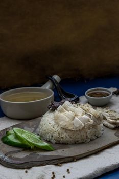 Hainanese chicken rice (Steam chicken with rice) with cucumber closeup on a plate and broth.
