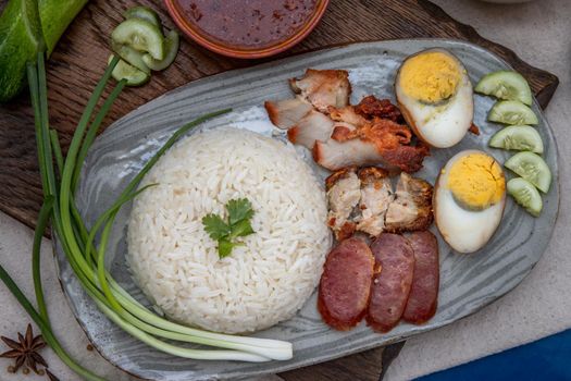 Red pork with rice (Kao Moo Dang) : Thai Style Red Barbecue Pork, duck egg and crispy pork belly, sliced cucumber with red sauce and broth. Horizontal top view