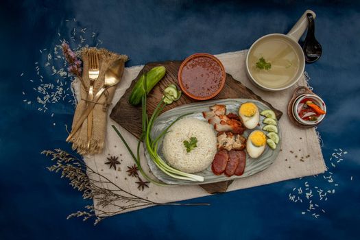 Red pork with rice (Kao Moo Dang) : Thai Style Red Barbecue Pork, duck egg and crispy pork belly, sliced cucumber with red sauce and broth. Horizontal top view