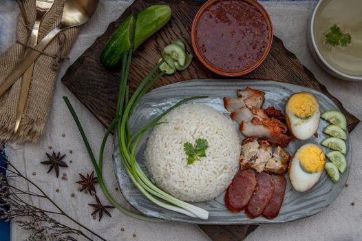 Red pork with rice (Kao Moo Dang) : Thai Style Red Barbecue Pork, duck egg and crispy pork belly, sliced cucumber with red sauce and broth. Horizontal top view