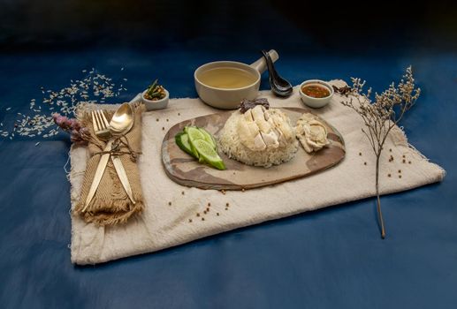 Hainanese chicken rice (Steam chicken with rice) with cucumber closeup on a plate and broth.