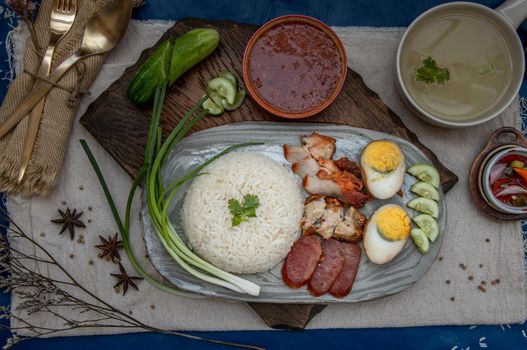 Red pork with rice (Kao Moo Dang) : Thai Style Red Barbecue Pork, duck egg and crispy pork belly, sliced cucumber with red sauce and broth. Horizontal top view