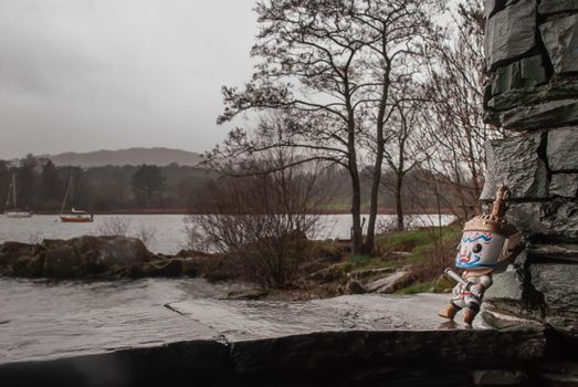 Ravana stood against a stone wall looking at the lake on a rainy day. Traveller doll.