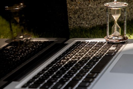 Hourglass on laptop keyboard. Time management concept and Countdown to deadline. Selective focus.