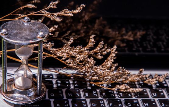 Hourglass on laptop keyboard. Time management concept and Countdown to deadline. Selective focus.