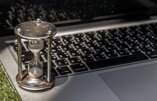 Hourglass on laptop keyboard. Time management concept and Countdown to deadline. Selective focus.