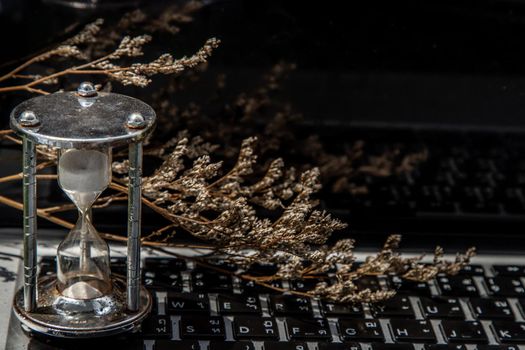 Hourglass on laptop keyboard. Time management concept and Countdown to deadline. Selective focus.