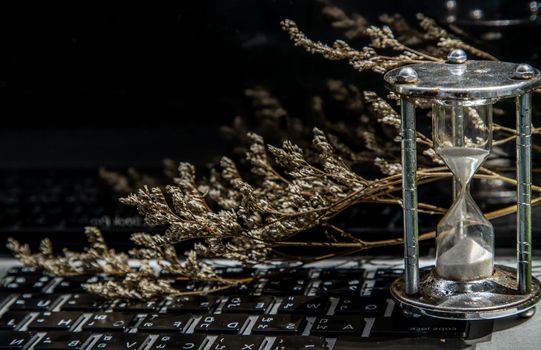 Hourglass on laptop keyboard. Time management concept and Countdown to deadline. Selective focus.