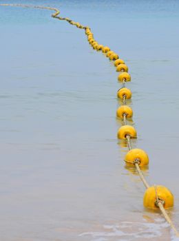 Chain of yellow polystyrene sea marker buoys with cable tow in blue sea water, in perspective