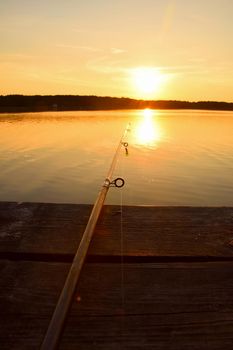 Close up high angle view of fishing rod on wooden pier at sunset hour, personal perspective